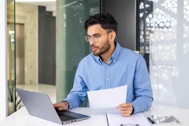 istock Focused young professional working on laptop and reviewing documents in modern office 2159516180