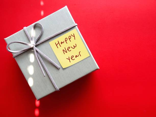 istock Simple minimal earth tone gift box on red copy space background with handwritten note HAPPY NEW YEAR, concept of joyful holiday festive season of gift giving, to family and love ones 2159516326