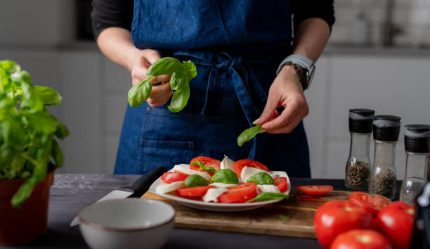 istock Woman Garnishes Caprese Salad With Basil 2159516653