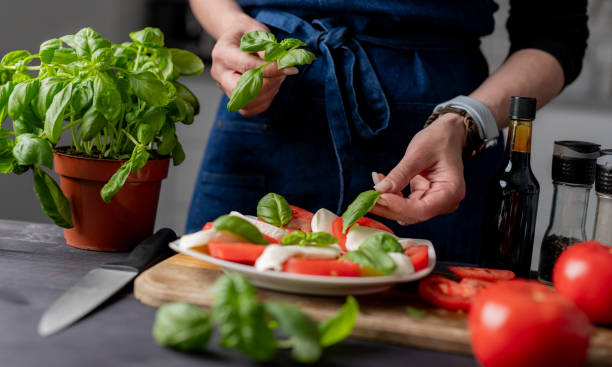 istock Woman Garnishes Caprese Salad With Basil 2159516762