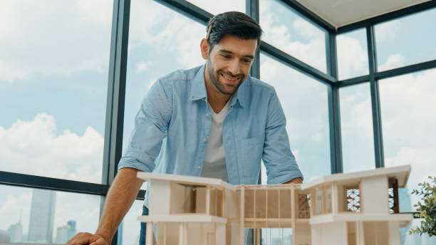 istock Portrait of engineer smiling at camera while inspect house model. Tracery 2159518143