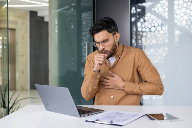 istock Man coughing in office while working on laptop, indicating stress or health issues 2159518339