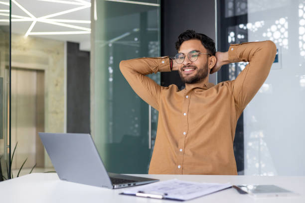 istock Young professional relaxing with hands behind head at modern office desk with laptop 2159518546