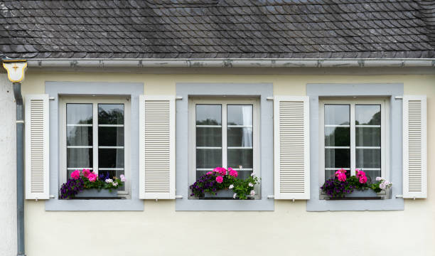 Open window on purple house wall with green shutters and flower pot.