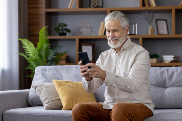 istock Senior man using a smartphone while sitting on a couch in a cozy living room 2159521331