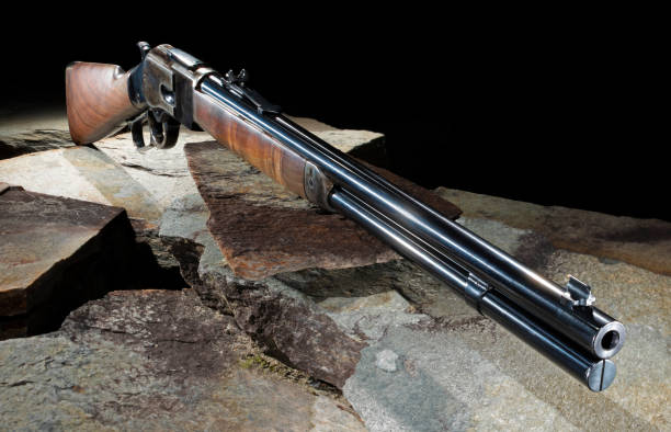 Rifle that is a lever action with a wood stock and blued steel on large flat stones with a black background.