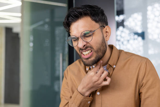 istock Man experiencing a sore throat, touching neck in discomfort inside modern office 2159522158