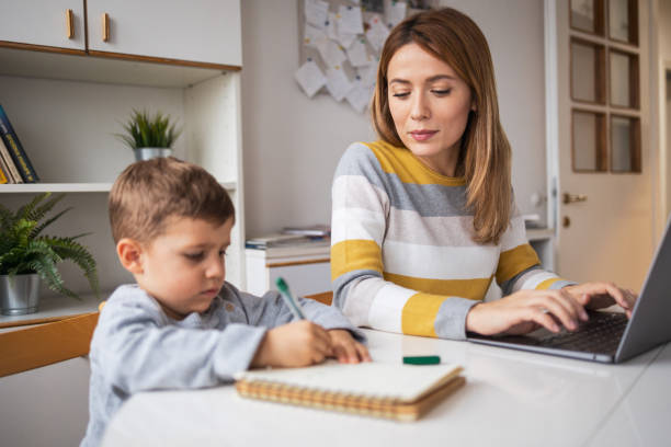 istock Working mother using laptop beside son writing in book at home 2159524565
