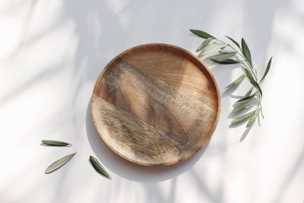 istock Summer wedding still life. Wooden plate, tray in sunlight. Olive tree branches on white table background i sunlight. Shadow floral overlay, dappled light.. Festive table setting. Flat lay, top view. 2159526983