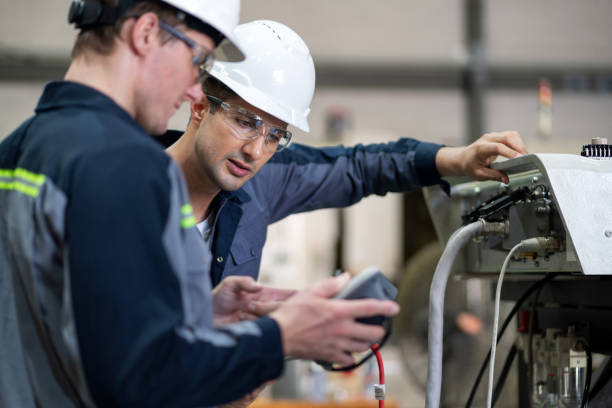 istock Engineers Operating and Inspecting Robotic Arm in Manufacturing Facility. Engineer checks connections and systems according to programmed commands in a manufacturing plant. 2159527436