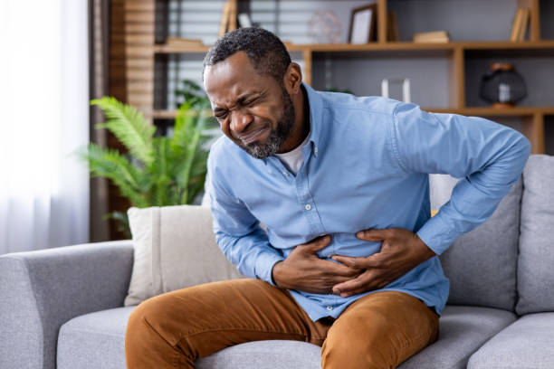istock Man experiencing stomach pain while sitting on a sofa in a living room 2159541609