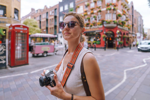 London tourist woman on Trafalgar Square taking photo holding camera smiling happy laughing having fun. Beautiful multiracial Asian Caucasian girl on travel vacation in London, England, United Kingdom