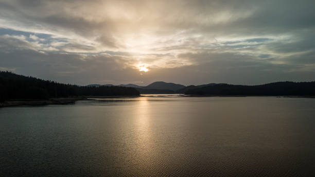 istock Sun shining through clouds over lake and forest at sunset 2159546222