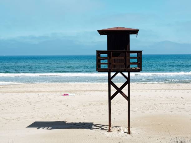 A lifeguard tower on an empty beach with a blue sky and calm ocean waves in the background.