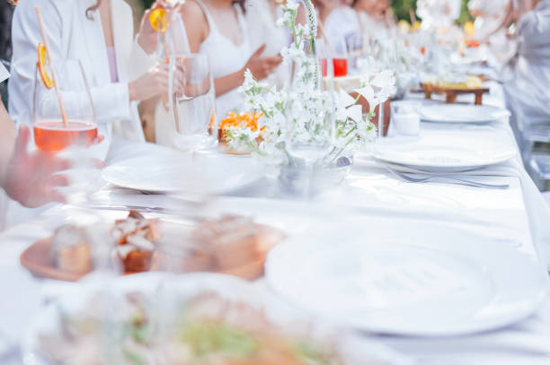 istock A festive covered table with a tablecloth with cutlery, decorated with flowers. Delicious snacks and glasses with drinks. People in white fancy clothes. 2159551601