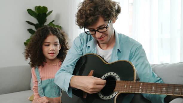 istock Father teaching daughter about playing guitar while sitting on sofa. Pedagogy. 2159555685