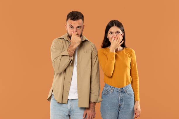 istock Two People Posing Silly With Hand Over Nose Against Orange 2159555758