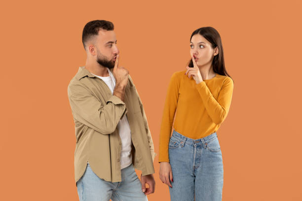 istock Young Man and Woman Gesturing Silence Against an Orange Background 2159555764