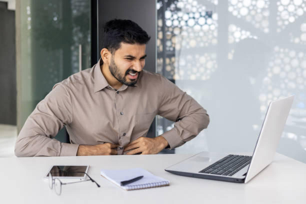 istock Businessman experiencing stomach pain while working on a laptop in office setting 2159556941