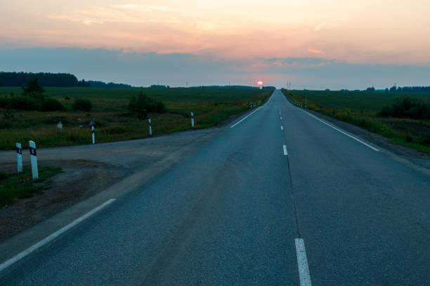an asphalt road leading to the horizon, sunset and sun in the sky