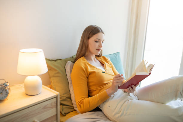 istock Pretty Girl Sitting on Bed Reading Book 2159561074