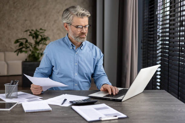 istock Mature businessman working at desk on laptop with documents in modern office 2159563382