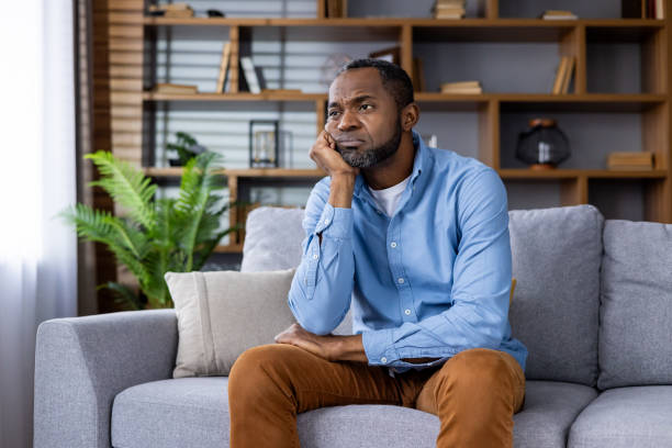 istock Man sitting on a couch looking thoughtful and pensive at home 2159565076