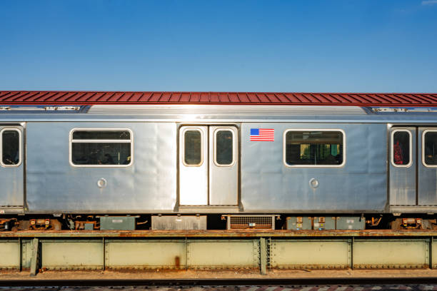This is a photograph of a subway train car viewed from an above ground platform on a sunny day with blue sky in the Bronx, New York.