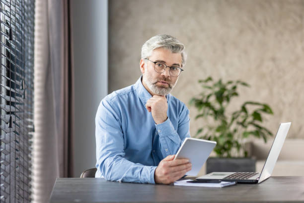 istock Mature businessman pondering over a decision while working with tablet and laptop in office 2159567405