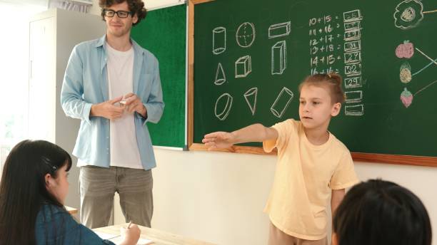 istock Smart boy pointing at diverse friend while children sitting at class. Pedagogy. 2159567436