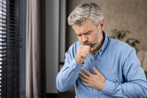 istock Elderly man coughing and holding chest with painful expression indoors 2159568708