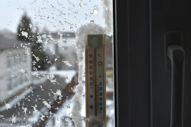A round thermometer is glued to a window pane and covered with snow, with condensation from the frost appearing on the window.