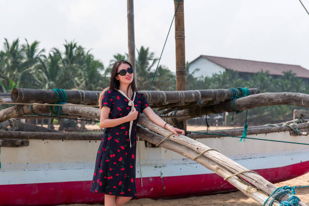istock Woman posing by a traditional boat on sandy beach with palms. 2159571304