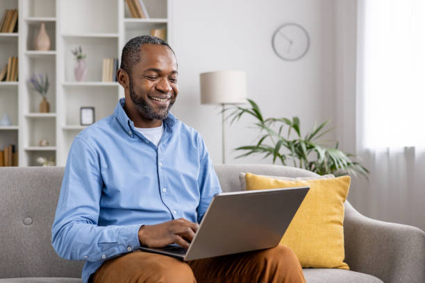 istock Smiling man working on laptop at home office while sitting on a couch 2159571320