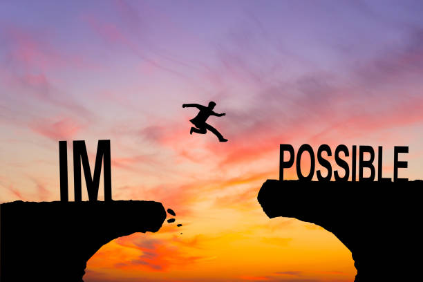 istock Mindset concept, Silhouette man jumping over impossible and possible wording on cliff with cloud sky and sunlight. 2159571717