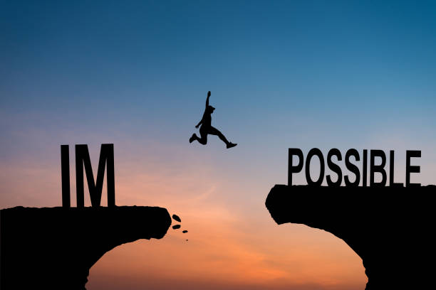 istock Mindset concept, Silhouette man jumping over impossible and possible wording on cliff with cloud sky and sunlight. 2159571738