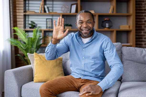 istock Smiling man happily waving while sitting on a comfortable sofa in a cozy living room setting 2159573205