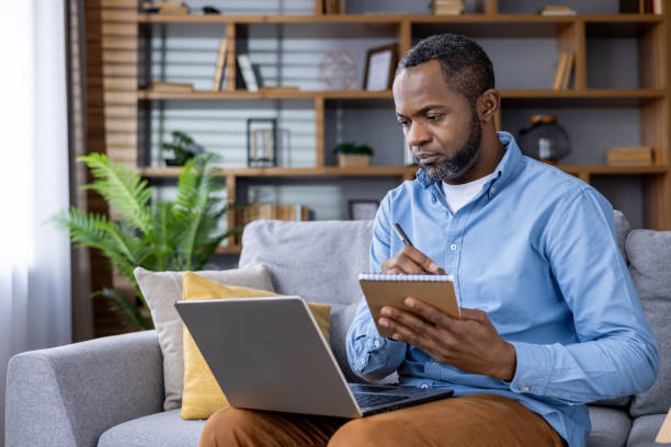 istock Man working from home on laptop taking notes in a living room 2159575336