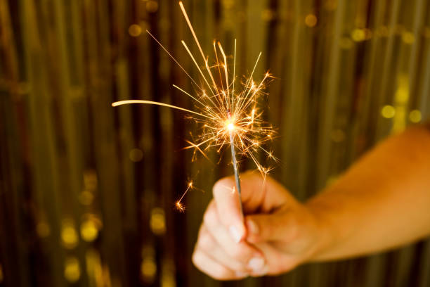 Close-up of hand holds a lit sparkler firework, glowing brightly. Moment for New Year and Christmas festivities.