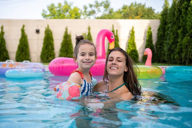 istock Mother and daughter having fun at the pool, while looking happily at the camera 2159578993