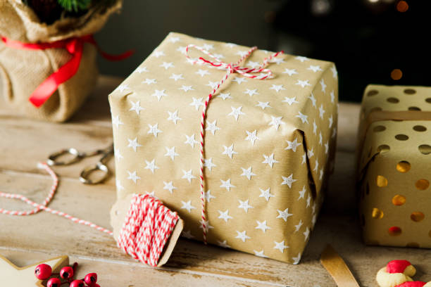 Wrapped Christmas gift box with tread on wooden table. Close-up of present box with golden wrapping paper and string on festive table.