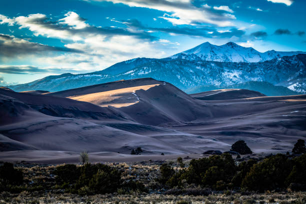 Great Sand Dunes National Park, Colorado, mountains with snow in the background, late afternoon ray of sunlight on one of the dunes.