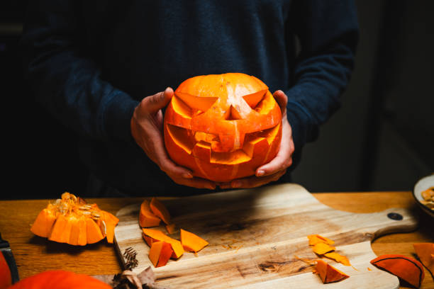 istock Man holding a creatively carved Jack O' Lantern above the kitchen counter 2159582468
