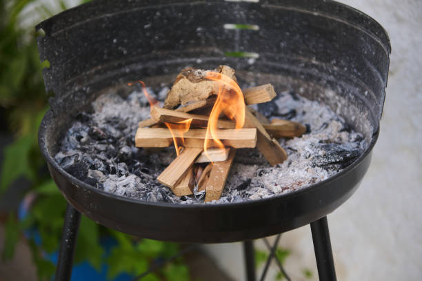 Close-up of wooden logs placed on a charcoal grill pit with a small flame burning. Ideal for outdoor cooking, barbecues, and creating a cozy atmosphere.