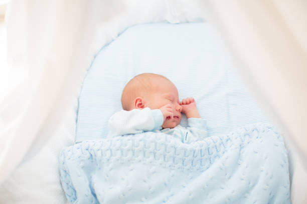 Newborn baby boy in bed. New born child sleeping under a blue knitted blanket. Children sleep. Bedding for kids. Infant napping in bed. Healthy little kid shortly after birth. Cable knit textile.