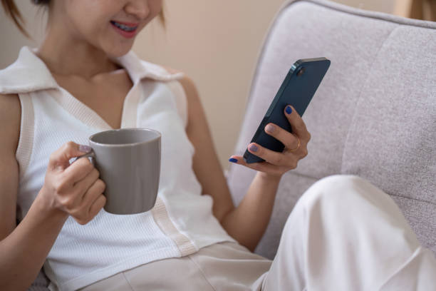 istock Young Woman Relax on Couch Using Smartphone and Drinking Coffee for Social Media Browsing 2159612818