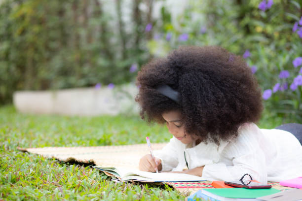 istock Child lying on mat on grass and drawing on notebook in garden, kid leisure doing activity hobby with drawing artistic in park, education and leisure in summer, education and learning concept. 2159615590