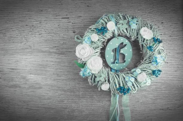 Decorative Easter wreath with flowers and a bunny ornament on a wooden background.