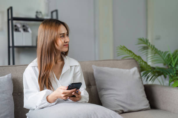 istock A woman is sitting on a couch with a cell phone in her hand 2159621581