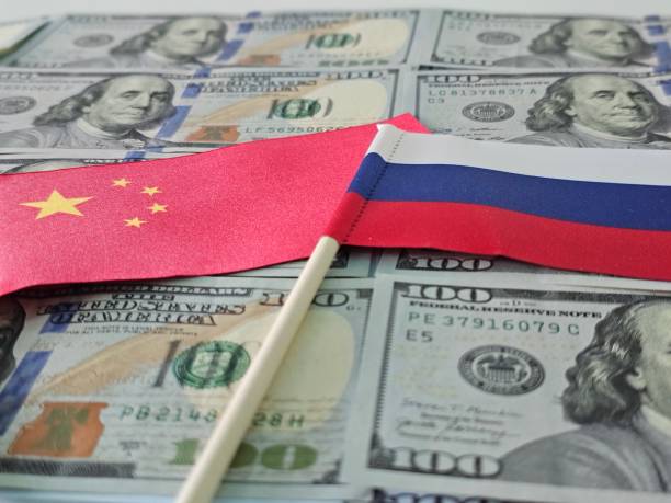 istock Chinese and Russian flags lying on a stack of US dollar bills concept 2159622415